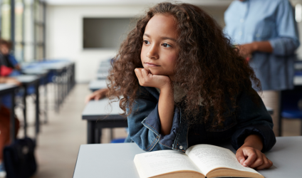 elementary school girl reading book at classroom desk